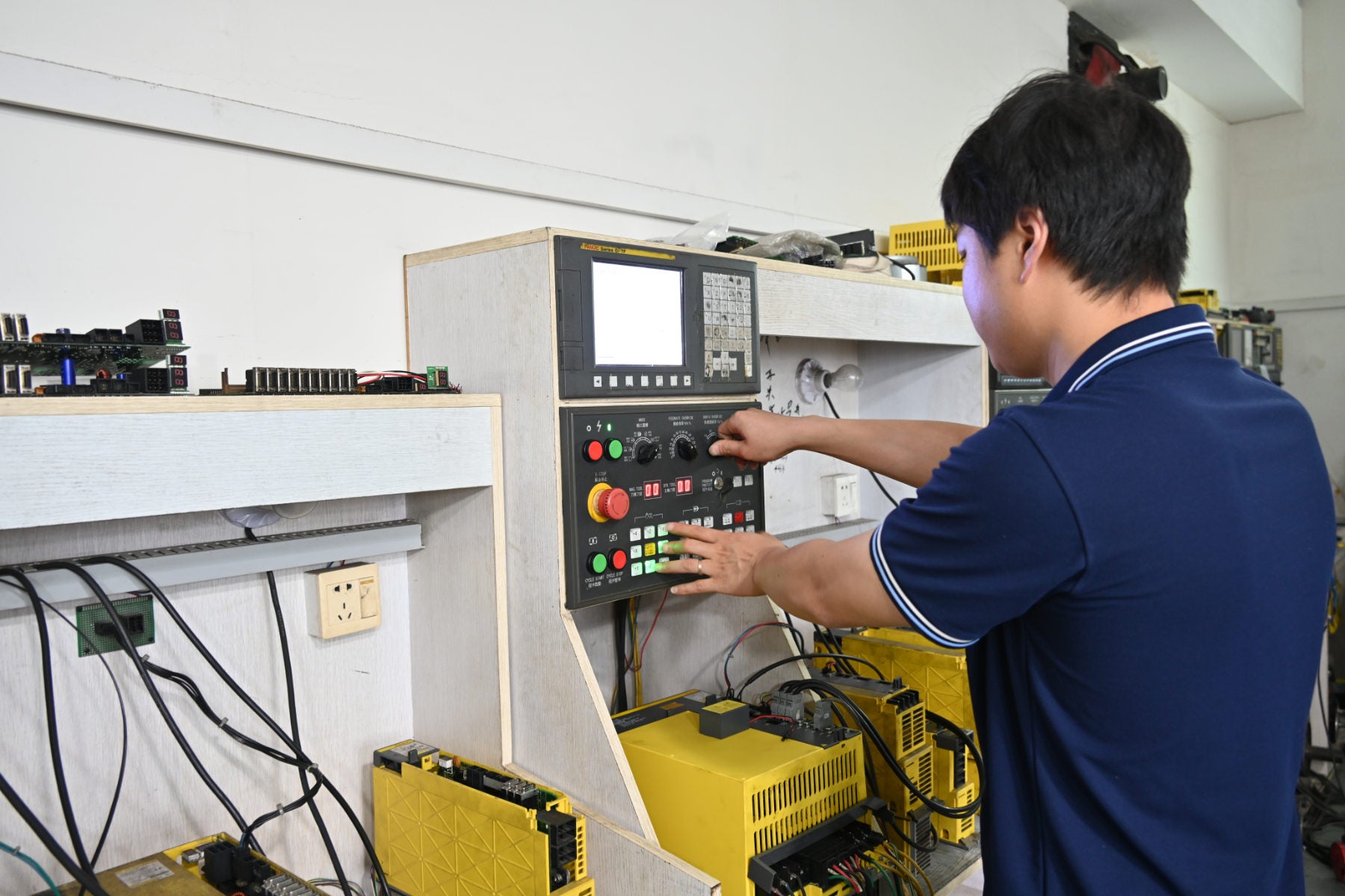 Technician operating FANUC CNC testing benches during system inspection and repair at REACO CNC.
