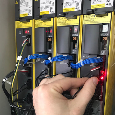 Technician inspecting and testing FANUC CNC drive modules during maintenance to ensure optimal performance.