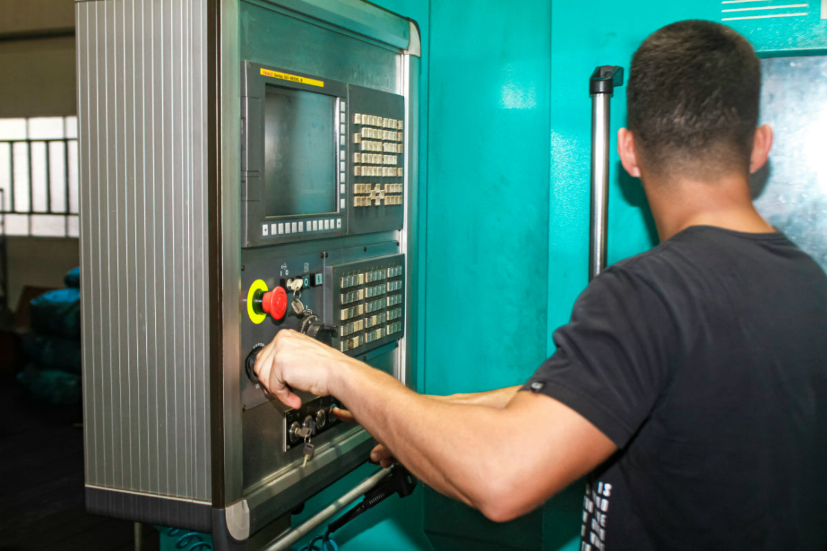 Technician operating CNC control panel for programming and monitoring machining process.